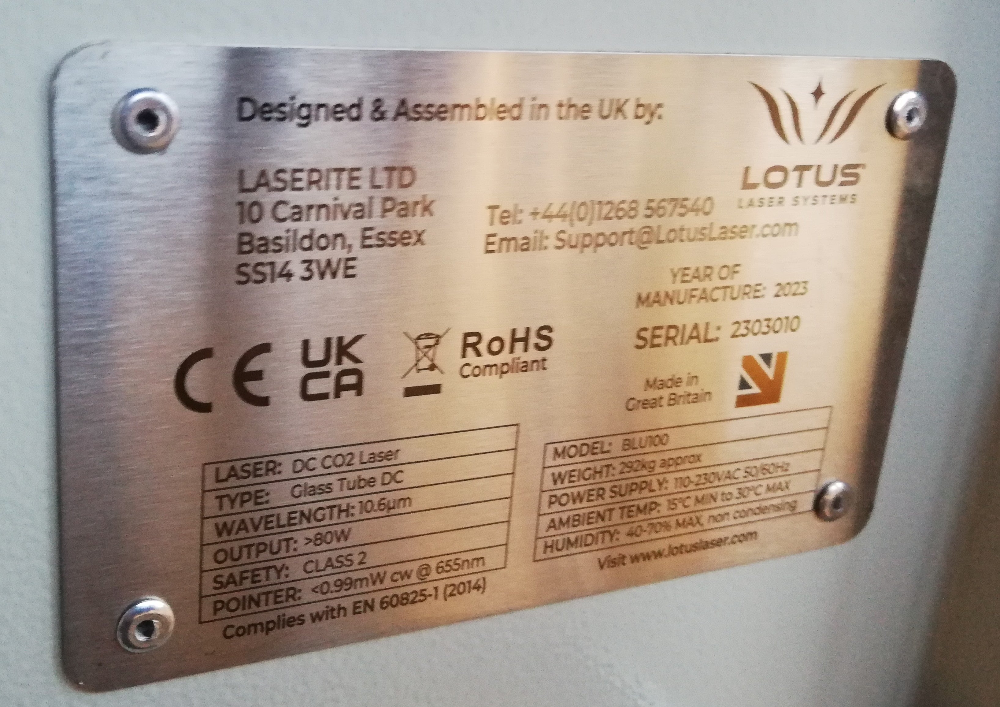 Silbernes Schild mit Maschineninformationen auf der Rückseite der Maschine mit Laser, Typ, Wavelength, output, Safety, Pointer, Model, Weight, Power Supply, Ambient Temp und Humidity.