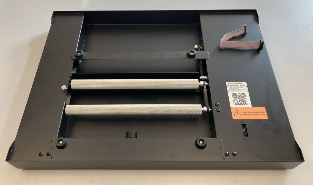 Rotationsaufsatz für Lasergravurmaschine mit zwei strukturierten Walzen, schwarzem Metallrahmen und Anschlusskabel.