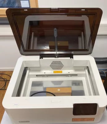 Geöffnete Flux Ador Maschine in weiß und schwarz mit Schneidbrett, Glashaube und Touchscreen.