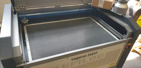 Geöffnete Epilog E9060 Legend 36 EXT Maschine in weiß und schwarz mit Schneidbrett, Glashaube, Not-Aus Knopf und Einstellungsmenu.