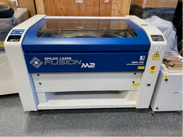 Epilog Fusion 40 M2 Maschine in Blau und Weiß mit Schneidtisch, Absaugschlauch, Glashaube, Einstellungsmenu, Rollen am Boden und Not-Aus Knopf.