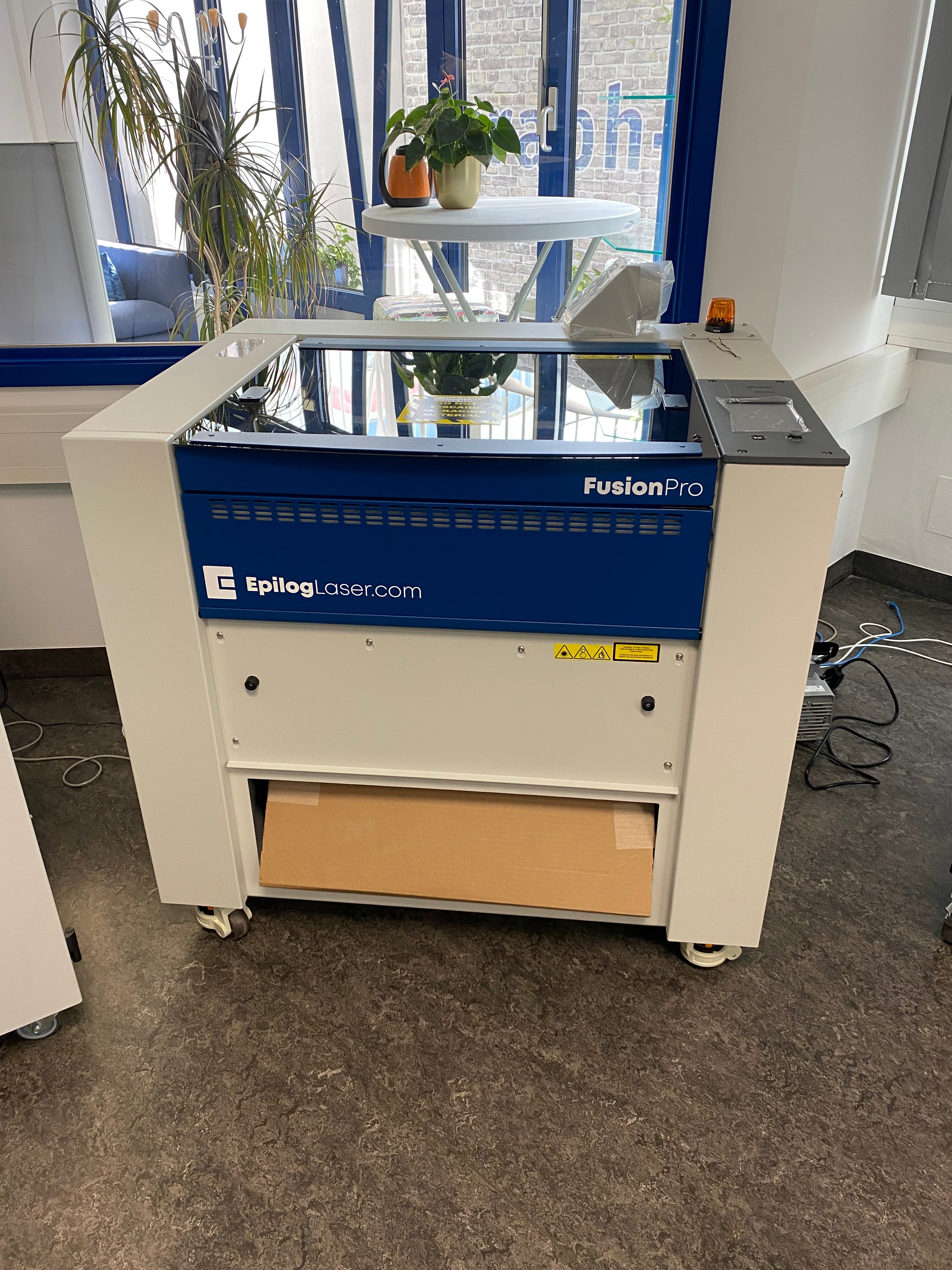 Epilog Fusion Pro 24 Maschine in Blau und Weiß mit Schneidtisch, Glasdeckel und Touchscreen.